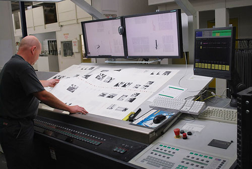 The pressman examining a first-pull test, surrounded by the controls of  the press's sophisticated colour and density management system.